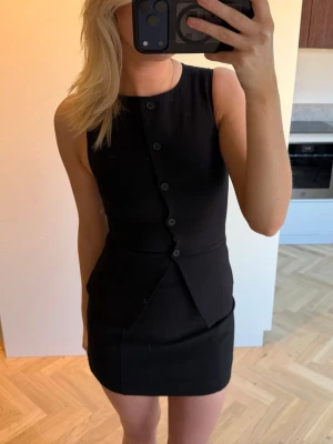 Gina Tricot - Svart kostymväst/topp - Svart kostymväst med knappar framtill. Toppen har en figurnära passform och är mindre över bysten. Aldrig använd och prislappen finns kvar.
