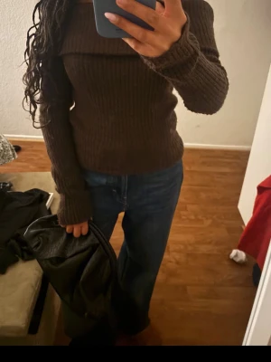 Brun off shoulder stickad tröja - Säljer en brun ribbstickad off shoulder-tröja med långa ärmar. Tröjan har en bred krage som kan bäras nedanför axlarna för en trendig look. Perfekt för dig som gillar en avslappnad men ändå stilren stil.