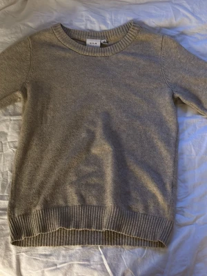 Beige stickad tröja från VILA - Mysig beige stickad tröja från VILA med rund halsringning och ribbade muddar vid ärmslut och nederkant. Enkel och stilren design som passar perfekt till jeans eller kjol.