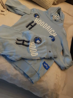 Ljusblå hoodie från Hoodrich - Snygg ljusblå hoodie från Hoodrich i storlek S. Hoodien har huva, ribbade muddar vid ärmar och nederkant samt vit text på bröstet. Tillverkad i mjukt och bekvämt material, perfekt för en chill och avslappnad stil. Se bilder för avvikelser, fläckarna är INTE tvättbehandlade/otvättad vid fotograferingen. 