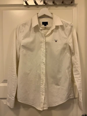 Vit skjorta från Gant - Klassisk vit skjorta från Gant med broderad logga på bröstet. Skjortan har lång ärm, knappar framtill och en tidlös krage. 