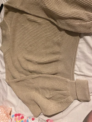 Beige ribbstickad tröja - Snygg beige ribbstickad tröja med breda muddar vid ärmslut och nederkant. Tröjan har en klassisk rund halsringning och är gjord i ett mjukt, tjockare material som passar perfekt för kyligare dagar. Enkel och stilren design som är lätt att matcha.