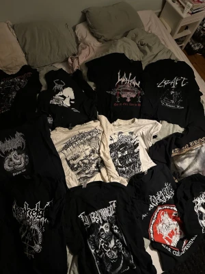 Black / death metal t-shirts - Samling av svarta och vita t-shirts med tryck från olika metalband. T-shirtsen har korta ärmar och grafiska motiv i vitt, rött och grått. Perfekta för dig som gillar metal och vill sticka ut med bandmerch. De flesta är i bomull och har klassisk passform.