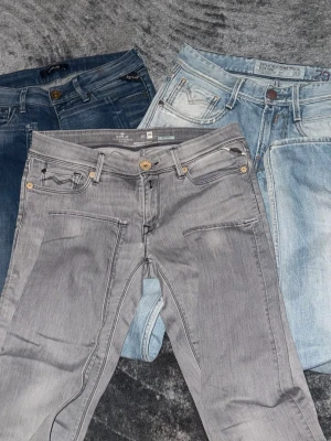 Tre par jeans i olika tvättar - Säljer tre par jeans från Replay i olika färger: ett par grå, ett par mörkblå och ett par ljusblå. Alla har klassisk femficksdesign, dragkedjegylf och snygga detaljer vid fickorna. Perfekta för dig som gillar stilrena och trendiga jeans.
