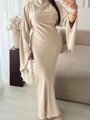 Beige långklänning med vida ärmar - Elegant beige långklänning med vida, fladdrande ärmar och hög hals. Klänningen har en figurnära passform som framhäver siluetten och är tillverkad i ett mjukt, slätt material. Perfekt för dig som vill ha en stilren och trendig look.
