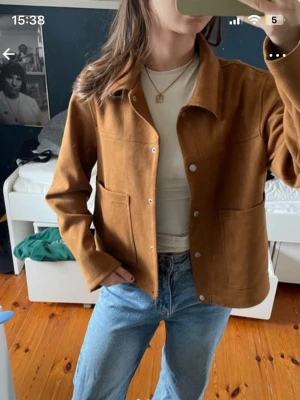 Brun overshirt med fickor - Snygg brun overshirt med klassisk krage och stora frontfickor. Jackan har raka ärmar och knäppning med silverfärgade tryckknappar. Materialet ser ut att vara mjukt och lite tjockare, perfekt för lager-på-lager. Passar till jeans och t-shirt för en avslappnad look.