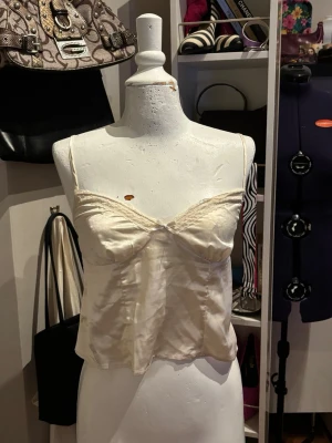H&M Satinlinne / Satin Camisole – Spetsdetalj – Beige / Champagne – Strl 40 - Elegant satinlinne från H&M i en mjuk beige/champagnefärg med fina spetsdetaljer vid bysten. Det glansiga satinliknande tyget ger en feminin och stilren look. Perfekt att bära både till vardags med jeans eller mer uppklätt till fest. Ett klassiskt plagg som passar i många outfits.