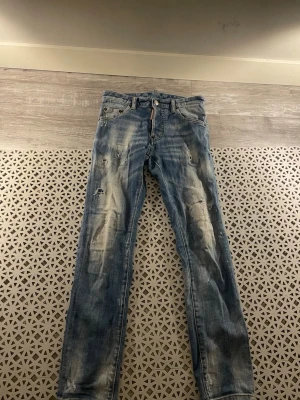 Dsquared 2 jeans  - Säljer ett par blå jeans med coola slitningar och distressed detaljer framtill och baktill. Jeansen har raka ben och klassisk femficksmodell. Perfekta för en avslappnad och trendig streetstyle-look.
