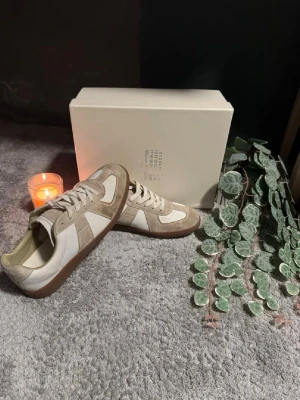  sneakers beige/vit - Säljer ett par sneakers i beige mocka och vitt läder. Klassisk low-top modell med gummisula och snygga detaljer. Perfekta för dig som gillar stilrena och tidlösa sneakers med premiumkänsla.