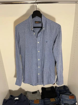 Blå mönstrad skjorta från Morris - Snygg blå skjorta från Morris med diskret mönster och klassisk krage. Skjortan har vita knappar och lång ärm. Hör gärna av dig vid frågor!