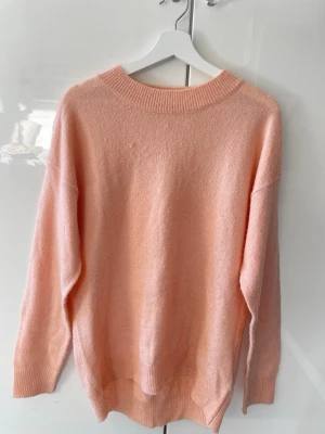 Ljusrosa/korallfärgad stickad tröja - Mysig ljusrosa/korallfärgad stickad tröja från Lager 157  i storlek M. Tröjan har rund halsringning, ribbade muddar och en avslappnad passform. Perfekt för lager på lager och ger en soft vibe till din outfit.