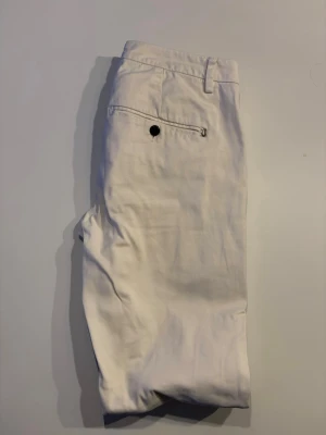 Vita chinos från Dondup - Snygga beige chinos från Dondup med klassisk passform. Byxorna har dragkedjegylf, bälteshällor och fickor fram samt en bakficka med knapp. Tillverkade i mjukt bomullstyg som ger en skön känsla och stilren look.