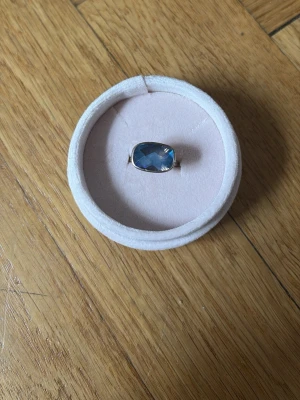 Silverring från KUMKUM med stor blå sten - Snygg silverring med en stor, rektangulär blå sten som fångar ljuset fint. Ringen har en enkel och stilren design som gör att stenen verkligen står i fokus. Perfekt för dig som vill ha ett statement-smycke med elegant touch.