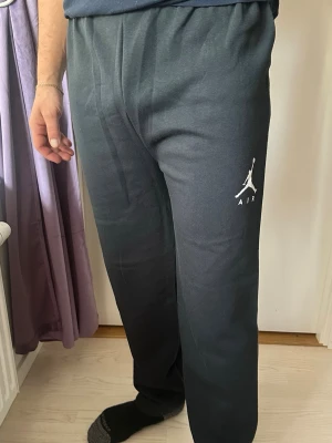Svarta Jordan Air mjukisbyxor - Säljer ett par svarta mjukisbyxor från Jordan med klassisk Air-logga tryckt i vitt på ena benet. Byxorna har resår i midjan och är tillverkade i mjukt och bekvämt material, perfekta för chill eller träning. Snygg och enkel design som passar till det mesta.