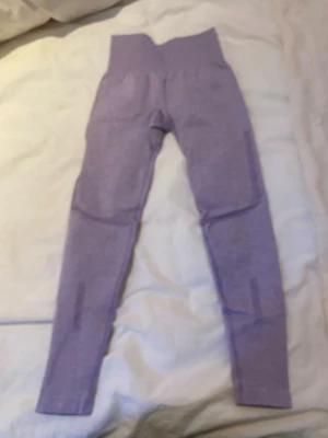 Lila sömlösa leggings med hög midja - Snygga lila leggings med hög midja och sömlös design. Materialet är stretchigt och följsamt, perfekt för träning eller chill. Diskreta mönsterdetaljer på benen och baksidan ger extra stilpoäng. Passformen är tight och bekväm.