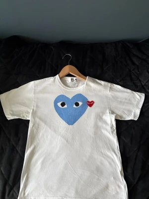 PLAY Comme des GARCONS T-shirt - Vit t-shirt från PLAY Comme des GARCONSmed ett stort blått hjärta med ögon och ett litet rött hjärta på bröstet. Klassisk passform och rund halsringning. Perfekt för dig som gillar grafiska tryck och vill sticka ut lite extra, T-shirten är i nyskick då jag knappast har använt den.