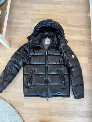  Moncler jacka  - Säljer en svart, glansig dunjacka från Moncler med huva och dragkedja framtill. Jackan har två fickor med dragkedja och Moncler-logga på ärmen.  Saknas kvitto därav priset 🤍 passar mig som är S men även min sambo som är en M! Kan skicka bild på om de behövs! Man gå ner i pris vid smidig affär 