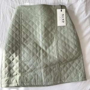 Quiltad leather ljusgrön kjol från NA-KD - Snygg quiltad kortkjol från NA-KD i en ljusgrön nyans. Kjolen har dragkedja bak och ett stilrent rutmönster. Perfekt att matcha med en enkel topp eller stickad tröja.