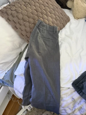 Grå kostymbyxor med raka ben - Snygga grå kostymbyxor med klassisk rak passform och pressveck. Byxorna har hällor för bälte och diskreta bakfickor. Perfekta för en stilren look. Materialet ser ut att vara en blandning av polyester och viskos. Använda 2 gånger