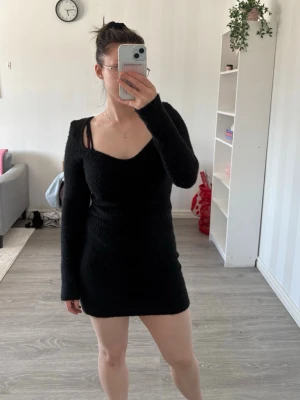 Svart stickad kort klänning - En svart stickad klänning med långärmar och v-ringad hals. Klänningen är kort och har en slim passform som framhäver figuren. Perfekt för dig som gillar en enkel och stilren look. Materialet är mjukt och bekvämt.