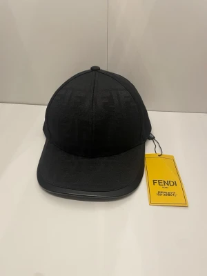 Svart keps från Fendi med FF-mönster - Snygg svart keps från Fendi med det klassiska FF-mönstret ton-i-ton över hela kepsen. Böjd skärm och justerbart band bak i läder med Fendi-logga. Tillverkad i textil med exklusiv känsla, perfekt för dig som gillar lyxiga accessoarer.