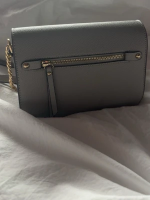 Grå väska - Grå väska med axelremsband som är köpt på en marknad💕har två fack inuti och 2 fläckar som syns, se sista bilderna