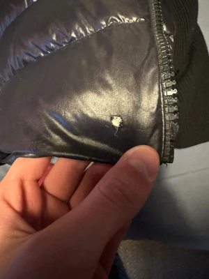 Svart pufferjacka från Moncler - Snygg svart pufferjacka från Moncler med glansig yta och stickade detaljer. Jackan har en ficka med lock och Moncler-logga på ärmen. Materialet är en mix av glansigt tyg och stickat, perfekt för kalla dagar.