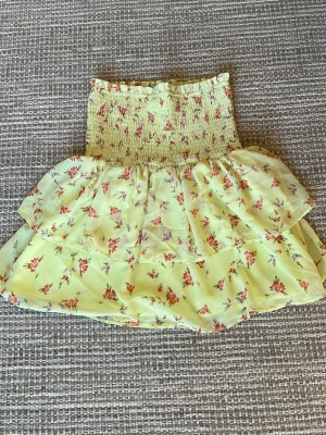 Gul blommig volangkjol - Supersöt kort gul kjol med blommigt mönster i rosa och lila. Kjolen har bred smock i midjan och dubbla volanger för extra flowy känsla. Perfekt för varma dagar och ger en romantisk vibe. Går att använda både som kjol och överdel. Använd max 3 gånger. Pris kan diskuteras