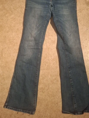 Blå bootcut jeans - Ett par klassiska blå bootcut jeans i denim med lätt slitna detaljer och rå kant längst ner. Jeansen har normal midja och fickor. Perfekta för en avslappnad och trendig look.