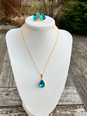 Smyckesset Pear Aquamarine  - Ett set med halsband och örhängen med brisyrkrok i guldplätterad mässing och kristaller. Aurora pear 13x18mm färg Dark Aquamarine. Längd 48cm inkl lås och förlängningskedja.  Finns även att få i andra färger på kristallen.   Jag skickar endast spårbart, samfraktar. Fast pris. Besök gärna mina övriga annonser.  Till mina smycken använder jag kristaller från Preciosa, Aurora och Swarowski.