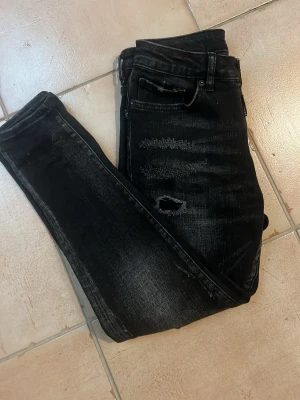 Dsquared 2 jeans  - Säljer ett par svarta slim jeans med slitningar och hål på låren och knäna.knappgylf och en tvättad look som ger en cool och trendig vibe. Perfekta för dig som gillar streetstyle och vill ha ett par bekväma jeans med attityd.