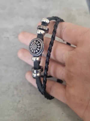 Svart flätat läderarmband med metallpärlor - Snyggt svart armband i flätat och slätt läder med silverfärgade metallpärlor och en rund dekoration med mönster. Justerbar knytning för perfekt passform. Perfekt accessoar för en cool och avslappnad stil.