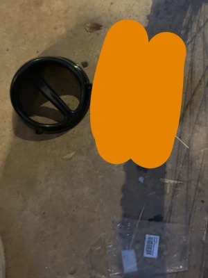 Svart plastventil rund - Rund svart ventil i plast, troligen för ventilation eller luftintag. Har två spjäll och monteringsfästen på sidorna. Passar till olika typer av installationer där luftflöde behöver regleras.