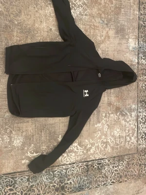 Svart jacka från Under Armour - Snygg svart jacka/windbreaker från Under Armour med dragkedja framtill och justerbar huva. Loggan sitter tryckt i vitt på bröstet. Tillverkad i ett mjukt och stretchigt material som känns skönt mot huden. Perfekt för dig som gillar sportig och clean stil. Priset kan diskuteras 
