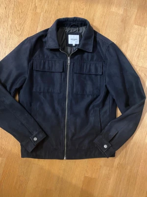 Mörkblå overshirt från Jack & Jones - Stilren mörkblå overshirt från Jack & Jones med klassisk krage, två stora bröstfickor och dragkedja framtill. Riktigt fet! Storleken är i S