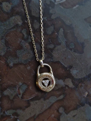 Michael Kors Halsband i Guldpläterat Silver  Fint skick! - Säljer ett stilrent Michael Kors-halsband med ett hängsmycke i form av ett hänglås prytt med gnistrande stenar. En modern klassiker som passar till allt! Halsbandet köptes under 2024 och är mycket sparsamt använt. Det är i jättefint skick, rent och utan skador. Givetvis äkta Michael Kors (modell MKC1573AN710).925 Sterling silver med 14K guldplätering.Tre cubic zirconia-stenar i mitten av låset. Mycket gott skick, väl omhändertaget.Observera: Säljes utan originalask och kvitto.