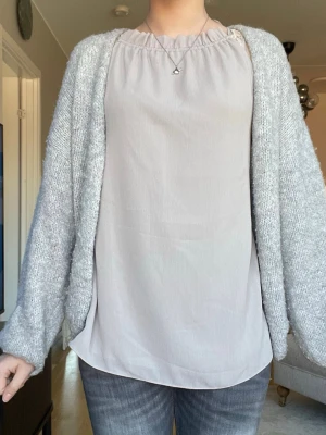 Beige blus med rynkad hals - Säljer en enkel och stilren beige blus med rynkad halsringning. Blusen är ärmlös och har en lös passform som ger en avslappnad look. Perfekt att matcha med jeans eller kjol för en trendig outfit.