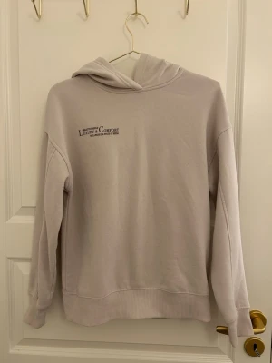 Ljusgrå hoodie Luxury & Comfort - Ljusgrå hoodie med tryck 'Luxury & Comfort' på bröstet. Mjuk och skön med huva och ribbade muddar vid ärmslut och nederkant. Perfekt för chill dagar och enkel att matcha med jeans eller mjukisbyxor.