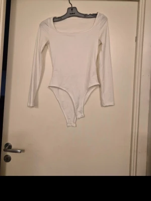 Vit långärmad body - Säljer en enkel och stilren vit body med långa ärmar och rundad urringning. Perfekt att matcha med jeans eller kjol. Tillverkad i mjukt stretchigt material för en bekväm passform.