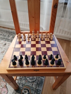 Schackspel i trä med pjäser - Snyggt schackspel i trä med klassiskt rutmönster i brunt och beige. Schackpjäserna är i svart och naturfärgat trä, och kungen är cirka 9 cm hög. Perfekt för dig som gillar strategi och brädspel.