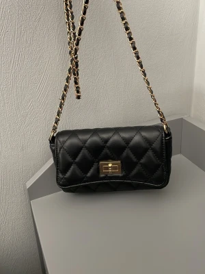 Axelremsväska  - Säljer en väska som aldrig har använts och som är i en utmärkt kvalitet. Väskan kan användas som en axelremsväska eller som en clutch om man lägger axelremmen inuti väskan. Väskan har även små fack