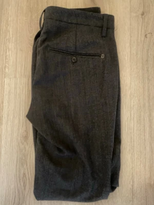 Dondup Mörkgrå chinos/kostymbyxor herr 33 - Snygga mörkgrå kostymbyxor med klassisk passform och diskret bakficka med knapp och dragkedja. Perfekta för en stilren look. Materialet känns mjukt och har en elegant struktur. Bälteshällor upptill för enkel styling.