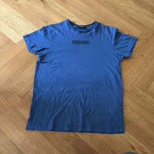 Blå DSQUARED2 t-shirt  - Blå t-shirt från DSQUARED2 med svart logotyptryck på bröstet. Tillverkad i mjuk bomull för en skön känsla. Skick:9/10✅. Passar cirka 156-167
