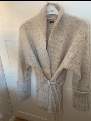 Beige stickad kofta med knytskärp - Mysig beige stickad kofta från Bikbok med ribbade muddar och knytskärp i midjan. 