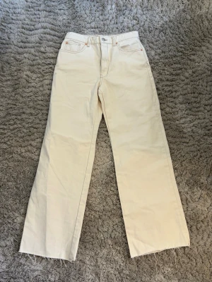 Vida raka jeans i offwhite - Säljer ett par vida raka jeans i offwhite med råa kanter nertill. Klassisk femficksmodell med bälteshällor. Jeansen har en enkel knappstängning och är tillverkade i kraftig bomull. Perfekta för en trendig look.
