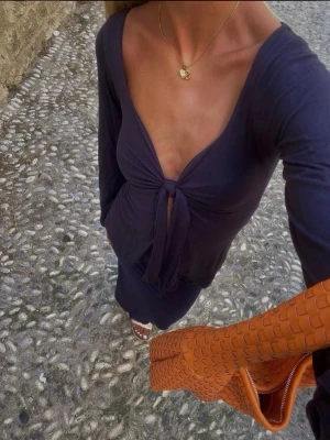 Mörkblå långärmad topp från design by si - Trendig mörkblå långärmad topp från Design by si med djup v-ringning och knytning framtill. Figurnära passform och mjukt, stretchigt material som ger en snygg siluett. Perfekt för dig som vill ha en stilren men ändå unik topp. Super fin till somnaren eller fest. Använd fåtalgånger.