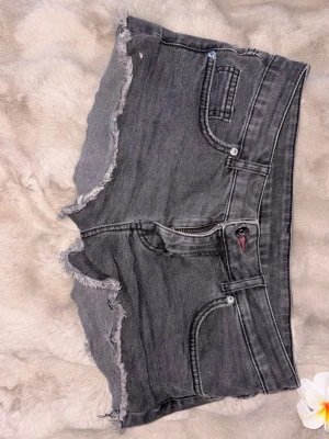 Grå jeansshorts med råa kanter - Säljer ett par grå jeansshorts fransiga kanter och klassiska fem fickor. Shortsen har dragkedja och knapp framtill samt  bakfickor med knapp. Perfekta för sommaren!❤️är M men skulle säg spadar s också!