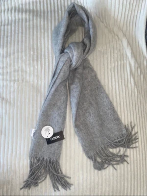 Ljusgrå halsduk  - Mjuk och stilren ljusgrå halsduk . Halsduken har klassiska fransar i ändarna och en enkel, avlång form som passar till de flesta jackor. Perfekt för att hålla värmen under kyliga dagar.