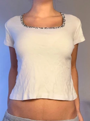 Vit croppad topp med leopardkant🤍 - Vit croppad topp med korta ärmar och fyrkantig ringning som har en snygg leopardmönstrad kant. Perfekt för en trendig och avslappnad stil. Tillverkad i mjuk bomull som känns skön mot huden.🤍