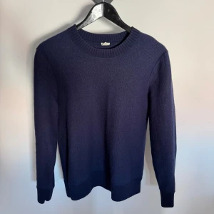 Mörkblå stickad tröja ARKET - En stilren mörkblå stickad tröja med rund halsringning och ribbade muddar vid ärmslut och nederkant. Perfekt för lager på lager och enkel att matcha med olika outfits. Klassisk passform och mjukt material.